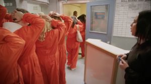 Inmates with hands on their head walking in orange jump suits